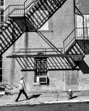 photo of a man walking by a wall with fire escapes